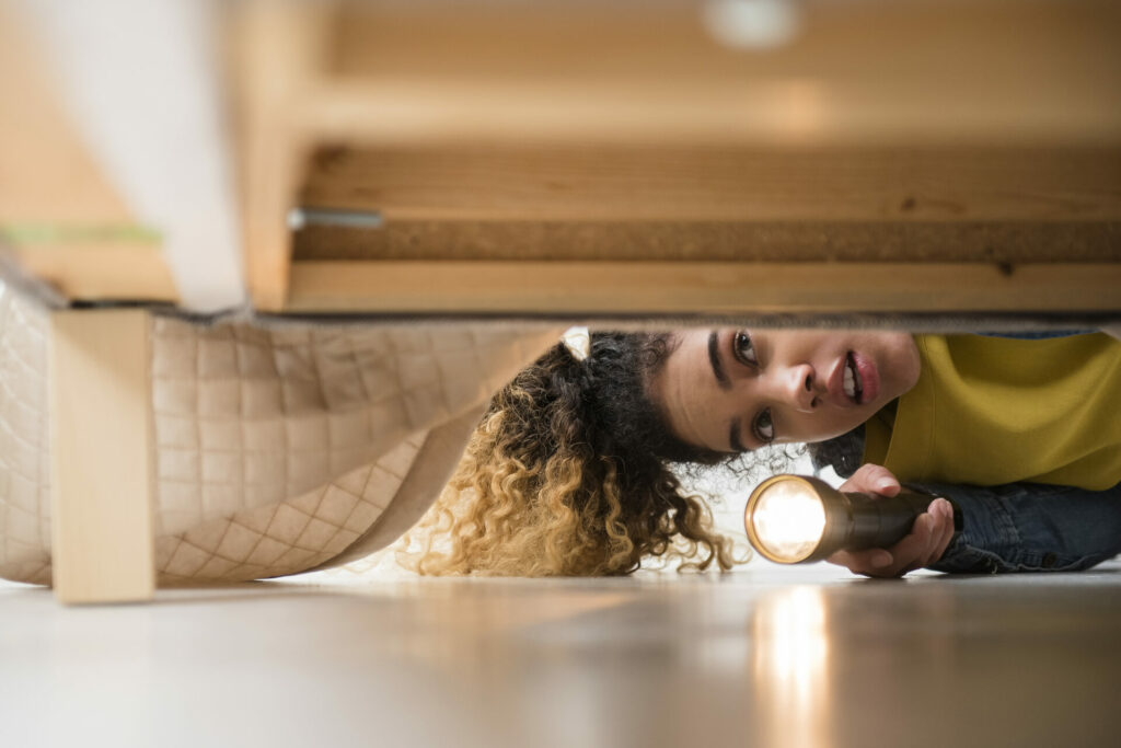 Frau keuchtet mit Taschenlampe unter das Bett